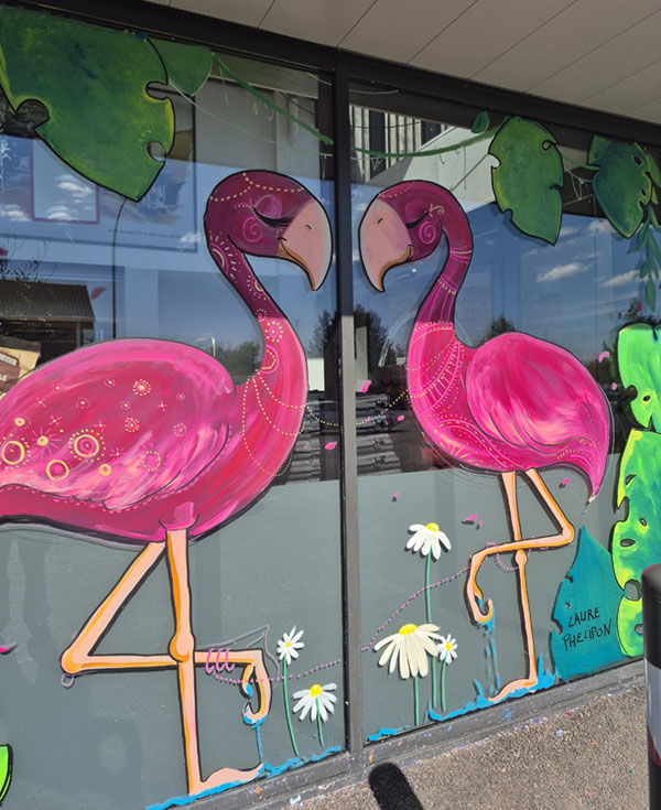 Détail de la fresque sur vitrine montrant deux flamants roses stylisés face à face, ornés de motifs dorés, entourés de fleurs et de grandes feuilles tropicales vertes.